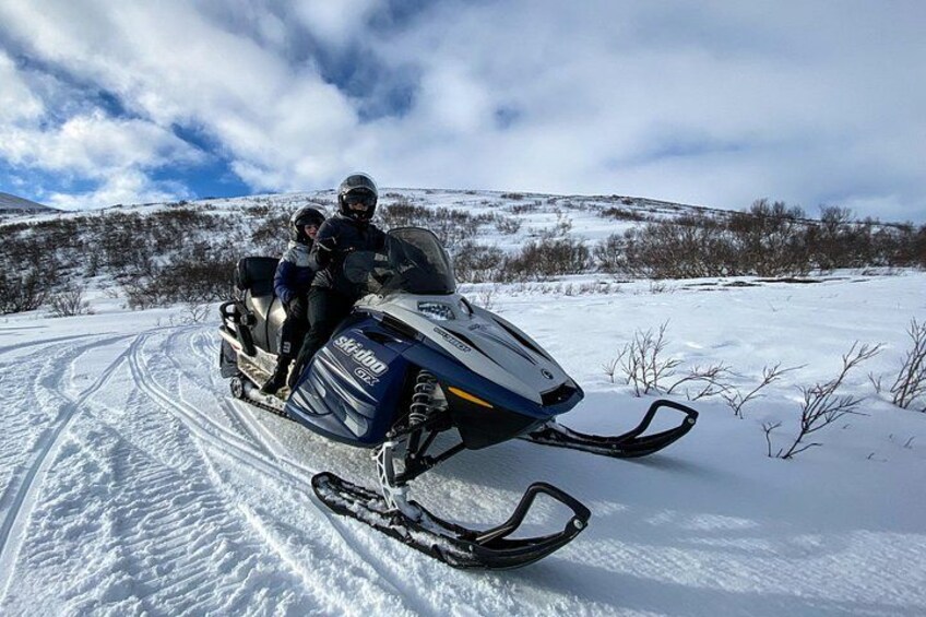A snowmobile on a snowy trail with a person and a child on board. 2