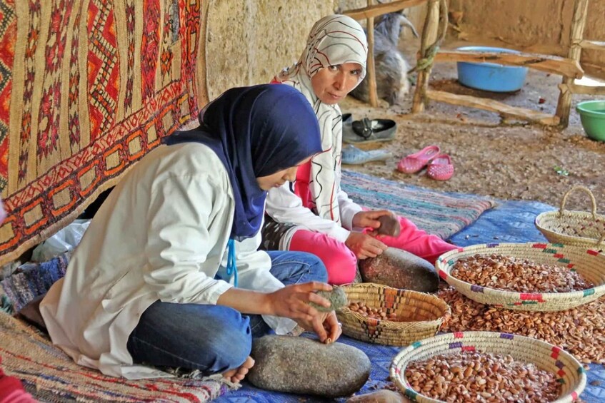Two women seated on a mat sorting beans. 4