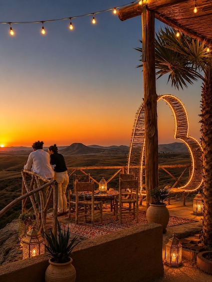 A sunset view with a wooden pergola, string lights, and a couple overlooking the landscape. 2