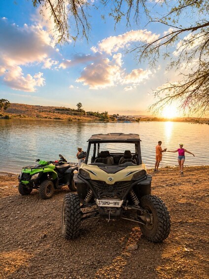A quad bike parked by a lake with people near the water. 5