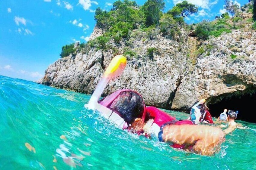 Une personne nage dans une eau turquoise et limpide, avec une côte rocheuse et une végétation luxuriante en arrière-plan. 4