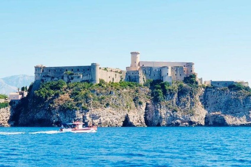 Un castillo costero en un acantilado, un barco en el agua y un cielo azul despejado. 2