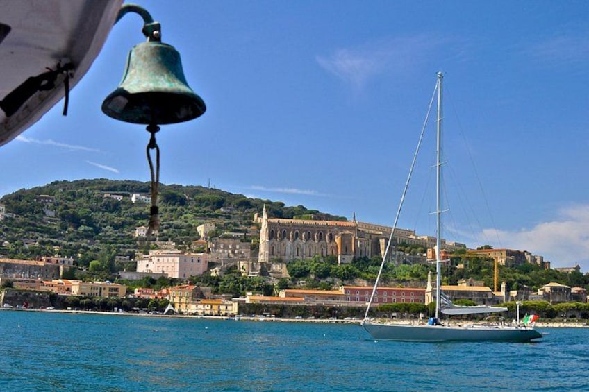 A sailboat on calm waters, a bell, and a historic building with a hill in the background. 5