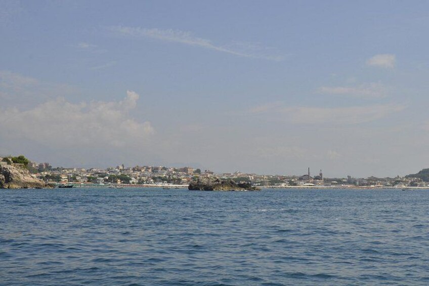 A coastal cityscape with calm waters, a rocky shoreline, and distant buildings. 4
