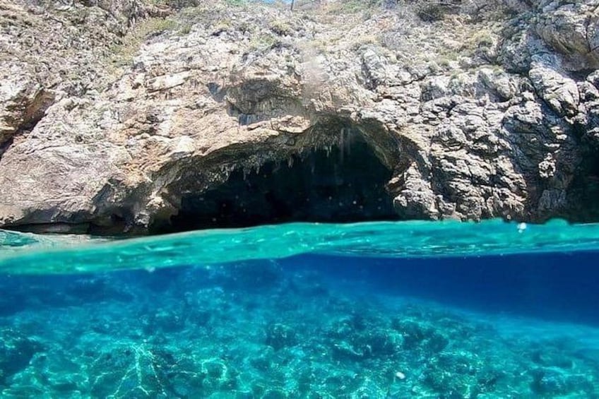 A rocky coastline with clear turquoise water and a cave entrance. 3