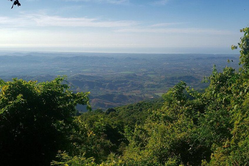 A mountainous landscape with dense green foliage and a distant view of a valley. 1