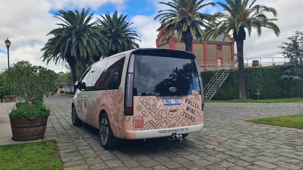 A white van parked on a cobblestone path with a license plate, surrounded by greenery and palm trees. 1