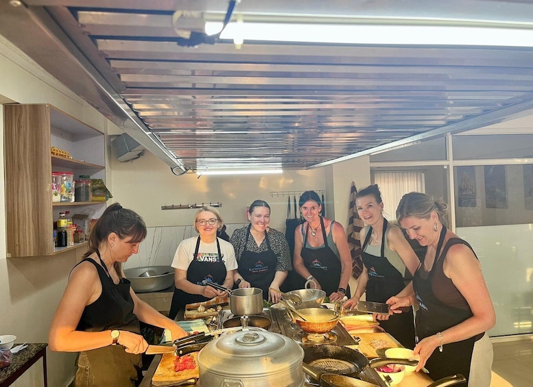 A group of people cooking in a modern kitchen with stainless steel appliances and wooden shelves. 5