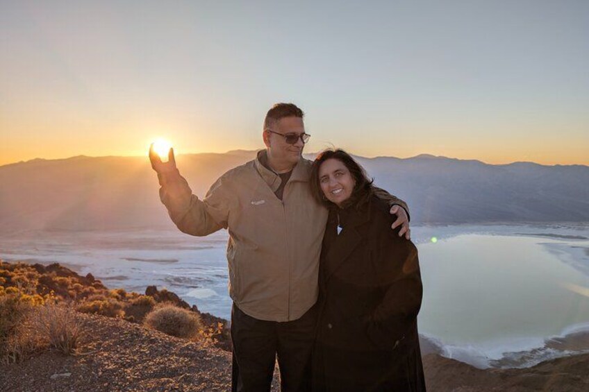 Una pareja está de pie sobre un terreno rocoso, con una masa de agua y montañas al fondo durante el atardecer. 5