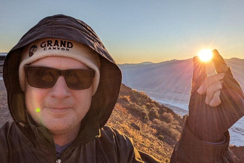 Una persona con una chaqueta que dice 'GRAND CANYON', sosteniendo una roca con el sol de fondo. 3