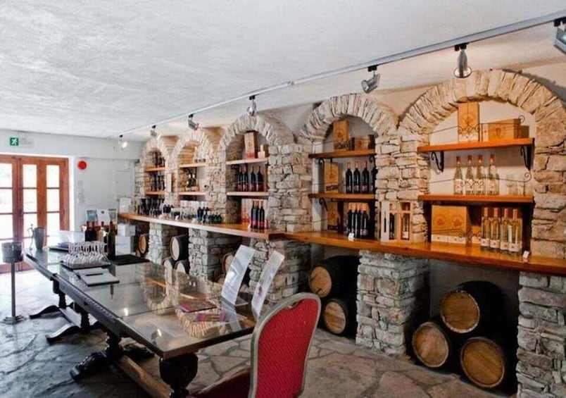 A bar with stone arches, wooden shelves with bottles, and a glass table. 4