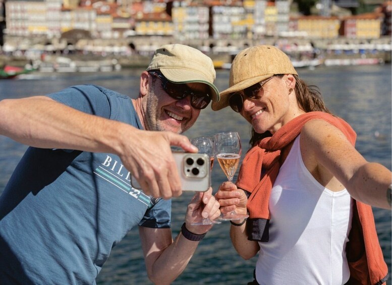 Two people taking a selfie with a smartphone, holding glasses of beer, and a waterfront background. 3