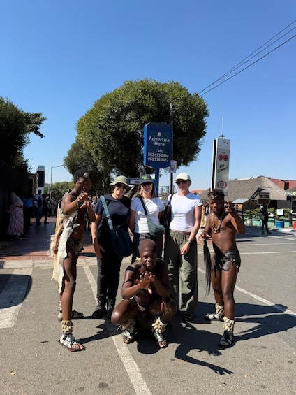 A group of people posing for a photo in an outdoor setting with a blue signboard and a large tree in the background. 1