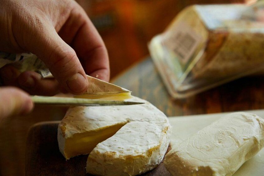A person cutting a wheel of cheese on a wooden board. 2