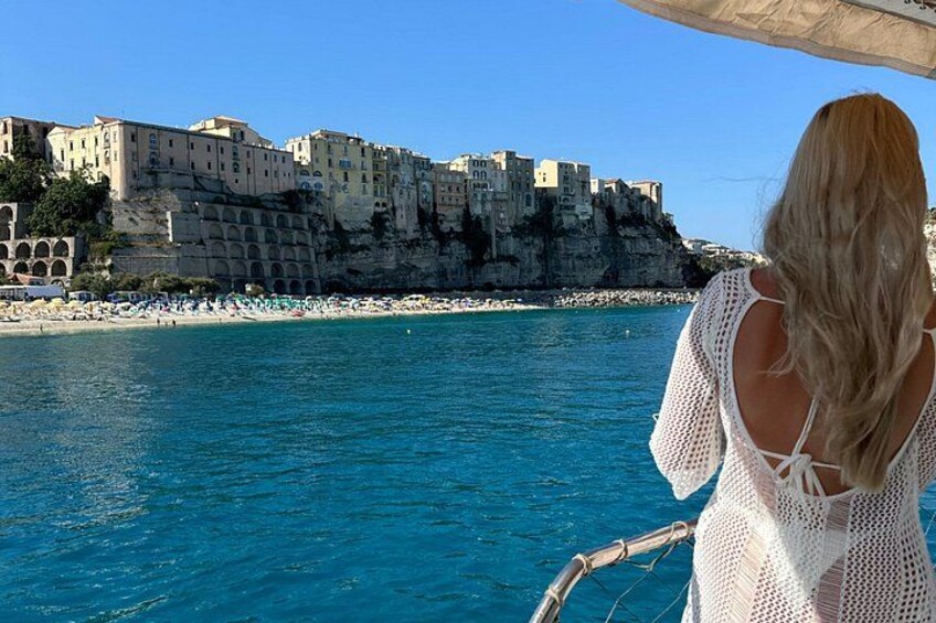 A coastal town with buildings on a cliff, a beach, and a boat with a person on it. 2