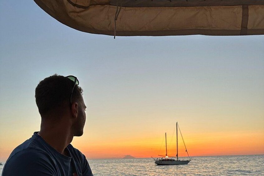 A person under a canopy overlooking a sunset with a sailboat on the water. 3