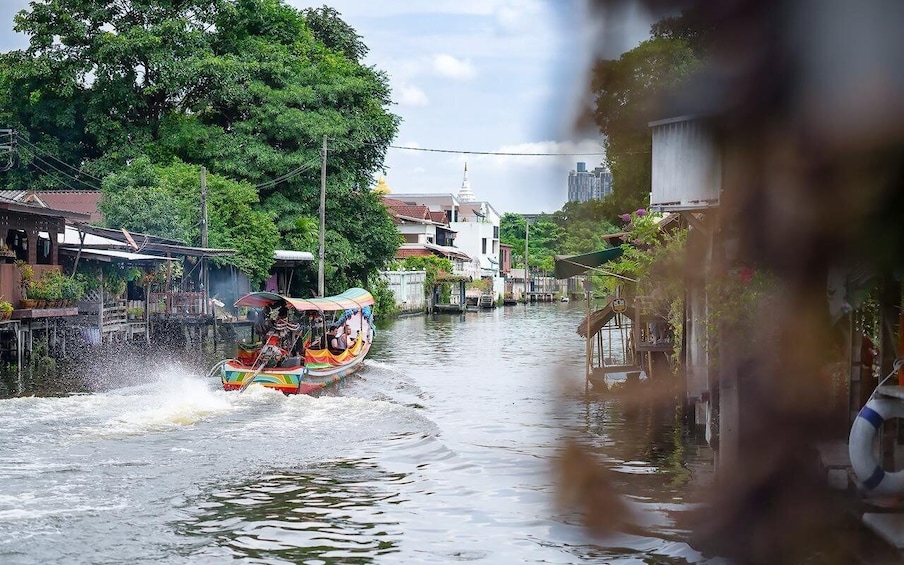 A colorful boat speeding through a narrow waterway flanked by buildings and trees. 5