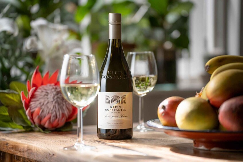 Eine Flasche Klein Konstantia Sauvignon Blanc, ein Obstteller und zwei Weingläser auf einer Holztisch. 4