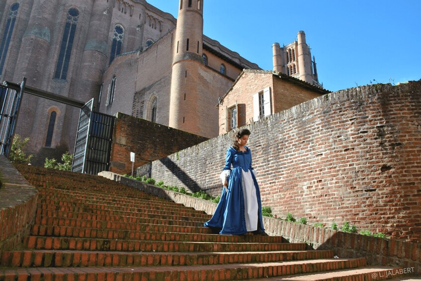 A person in historical costume descending a brick staircase with a church in the background. 3