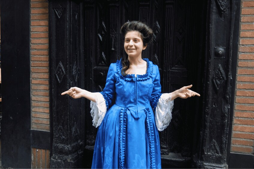 A person in a blue dress standing in front of a black door with a brick wall. 1