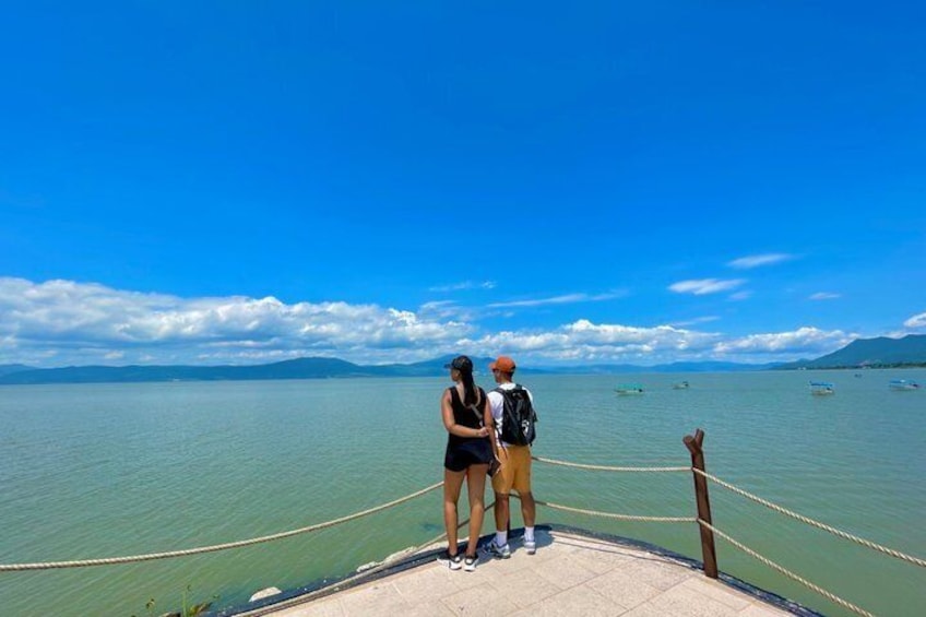 Two people standing on a dock with a view of calm water and distant mountains. 1