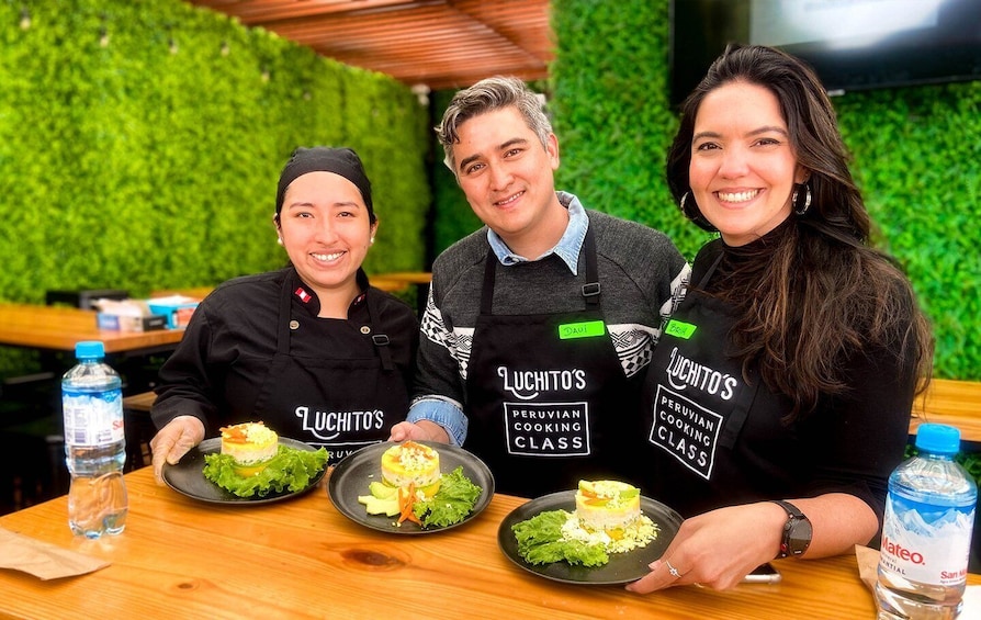 Tre persone con grembiuli con la scritta 'Luchitos Peruvian Cooking Class', che tengono piatti di cibo. 5