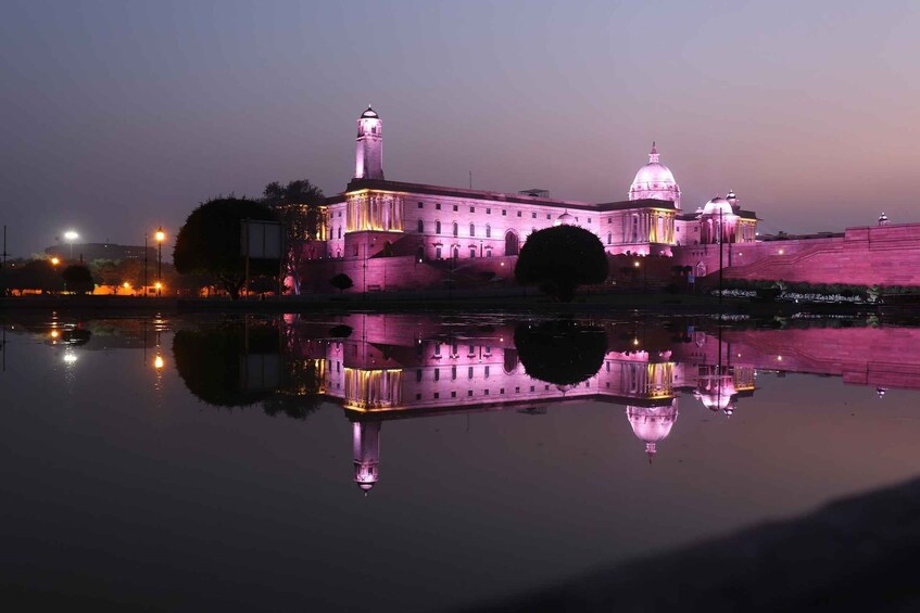 A large, illuminated building with a central dome and a tower, reflecting on a calm body of water. 2