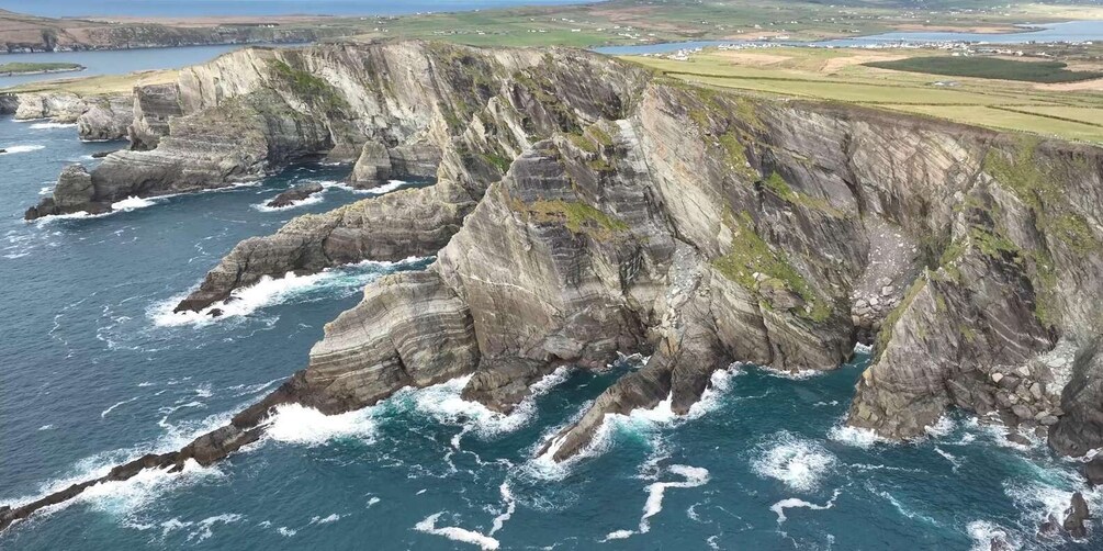 A coastal cliff with stratified rock layers and a turbulent sea. 2