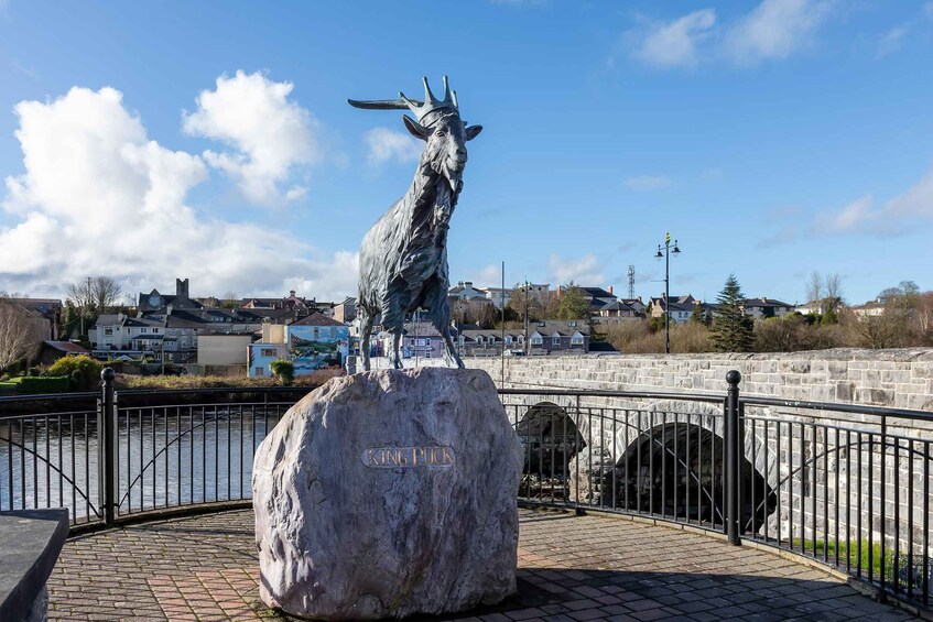A statue of a goat on a rock with 'KING PUK' inscribed, a stone bridge, and houses in the background. 5
