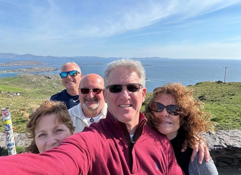 Eine Gruppe von Personen macht ein Selfie auf einem grasbewachsenen Hügel mit Blick auf das Meer und ferne Hügel. 5
