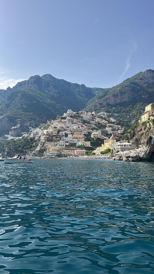 A coastal town with buildings on a hillside, a body of water in the foreground, and mountains in the background. 2