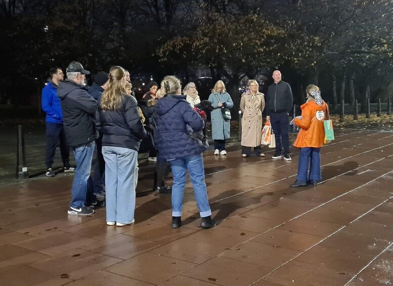 A group of people standing on a wet pavement in an outdoor setting at night. 4