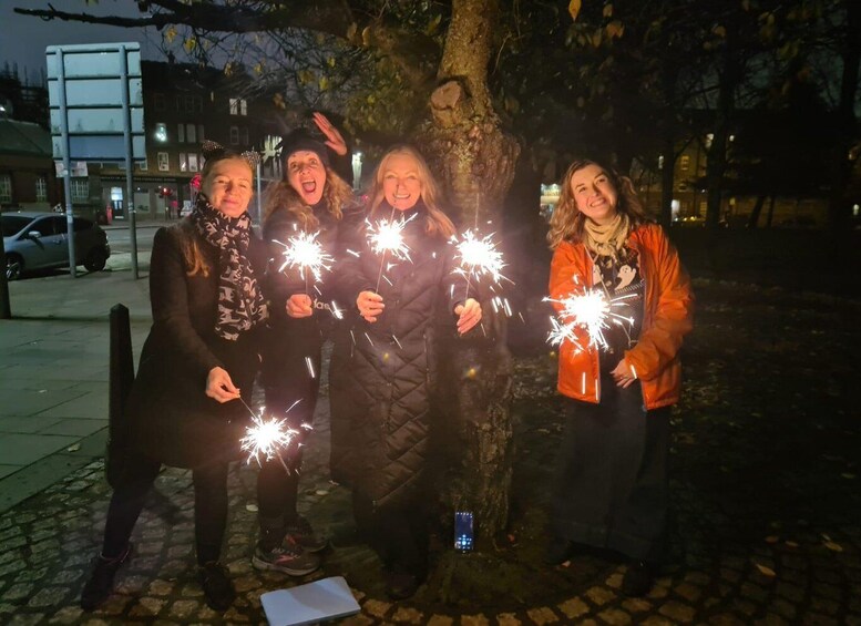 Four people holding sparklers near a tree on a sidewalk at night. 5