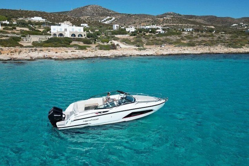 Un bateau à moteur blanc navigue sur une eau turquoise et limpide, avec un bâtiment blanc et des collines rocheuses en arrière-plan. 3