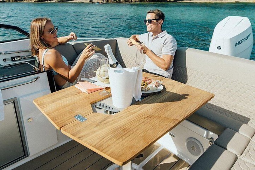 Deux personnes dînent sur un bateau, autour d’une table en bois, avec une glacière blanche et un moteur de bateau à proximité. 2