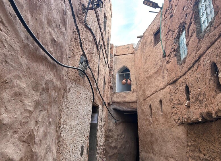 A narrow alley with traditional mud-brick buildings, a hanging light fixture, and a small window with pottery. 2