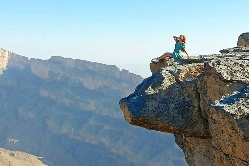 A person sitting on a rock formation with a canyon in the background. 1