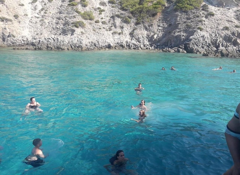 A group of people swimming in a clear blue sea with rocky cliffs in the background. 5