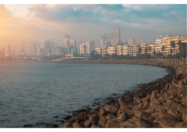 A coastal cityscape with a rocky shoreline, a bridge, and high-rise buildings under a cloudy sky. 2