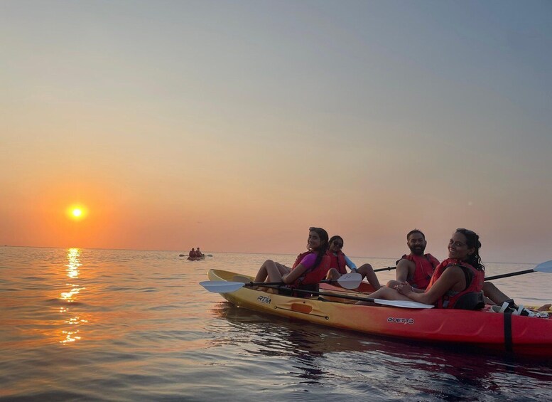 A sunset over calm waters with a group of people in a kayak. 1