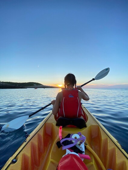 A person in a yellow kayak with a red life jacket paddling on calm water during sunset. 3