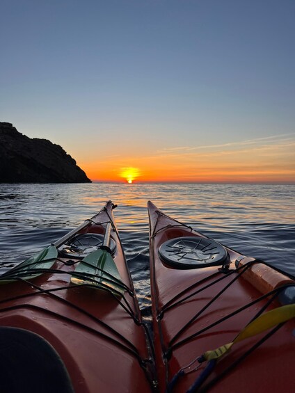 Two kayaks facing a sunset over calm water with a rocky coastline. 4