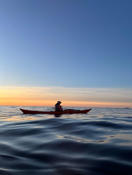 A person in a red kayak on calm water during sunset. 5