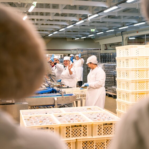 A group of people in a factory setting, wearing white protective clothing and gloves, working with machinery and materials. 1