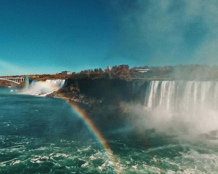 Ein Wasserfall mit Regenbogen, einer Brücke und bewaldetem Gebiet. 1