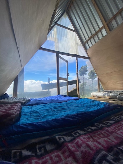 A tented accommodation with a bed, a view of the sky, and trees in the background. 4