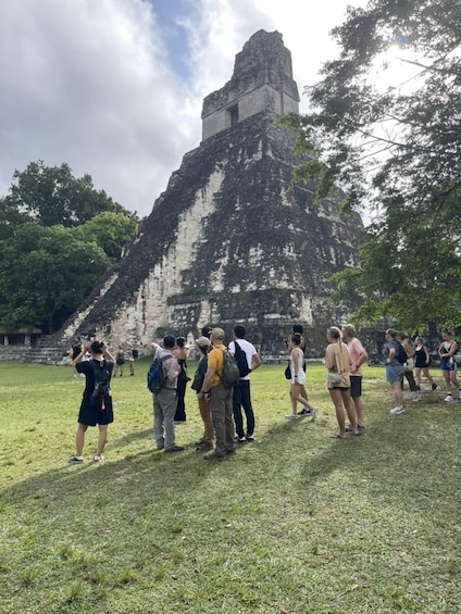 A group of people standing in a grassy area with a large ancient pyramid in the background. 3