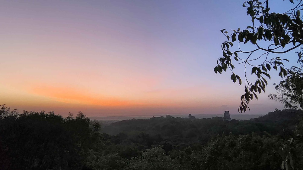 A sunset over a hilly landscape with dense vegetation and a distant structure. 2