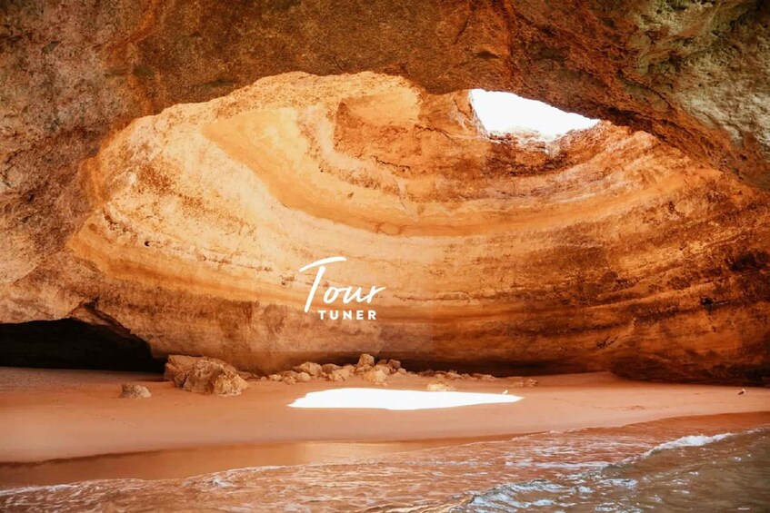A large, natural rock formation with layered colors and a beach in front. 3