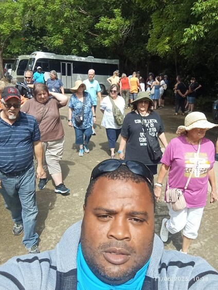 Un groupe de personnes se promène en plein air, avec des arbres et un autobus en arrière-plan. 2